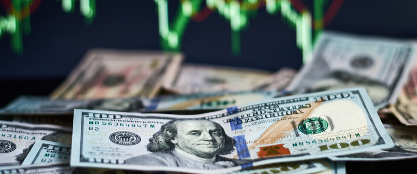 A substantial pile of dollar bills placed before a background board featuring intricate financial charts and data.