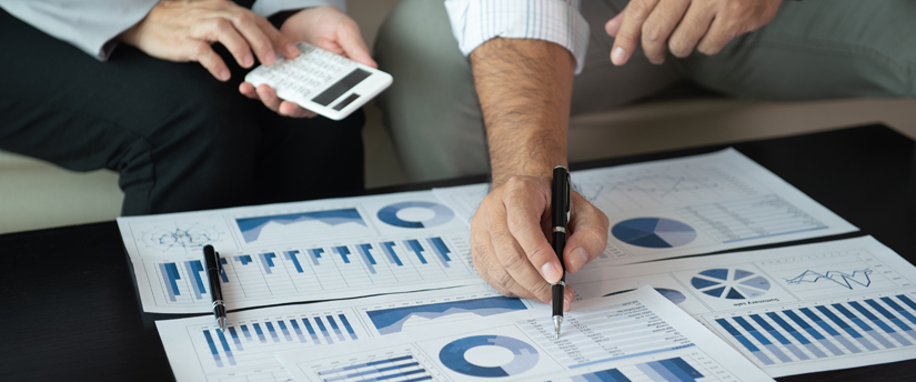 two men, one holding a calculator and the other one a pen, with some charts below, depicting fundamental analysis and reading the markets
