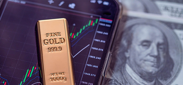 a small gold bar in front of a mobile scree with charts and a US dollar, referring to trading gold forex