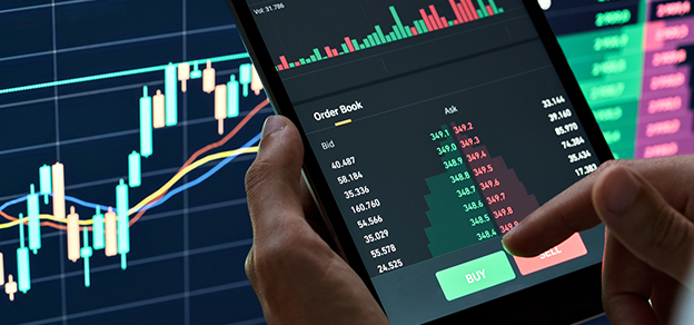 a man is checking Bid and Ask prices on a tablet and candlestick and line charts on a monitor which relate to how to buy stocks.