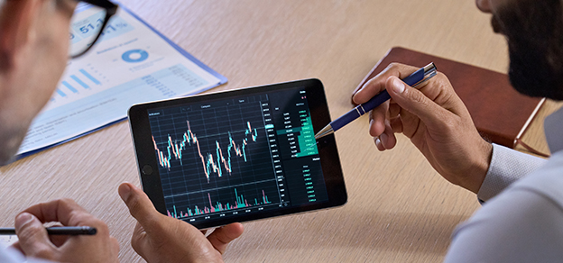 Two traders examining a tablet displaying forex data, embodying the essence of being forex traders.