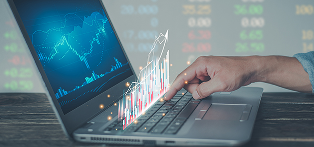 A trader, actively writing on their laptop while charts are displayed, searching for the best trading platform.