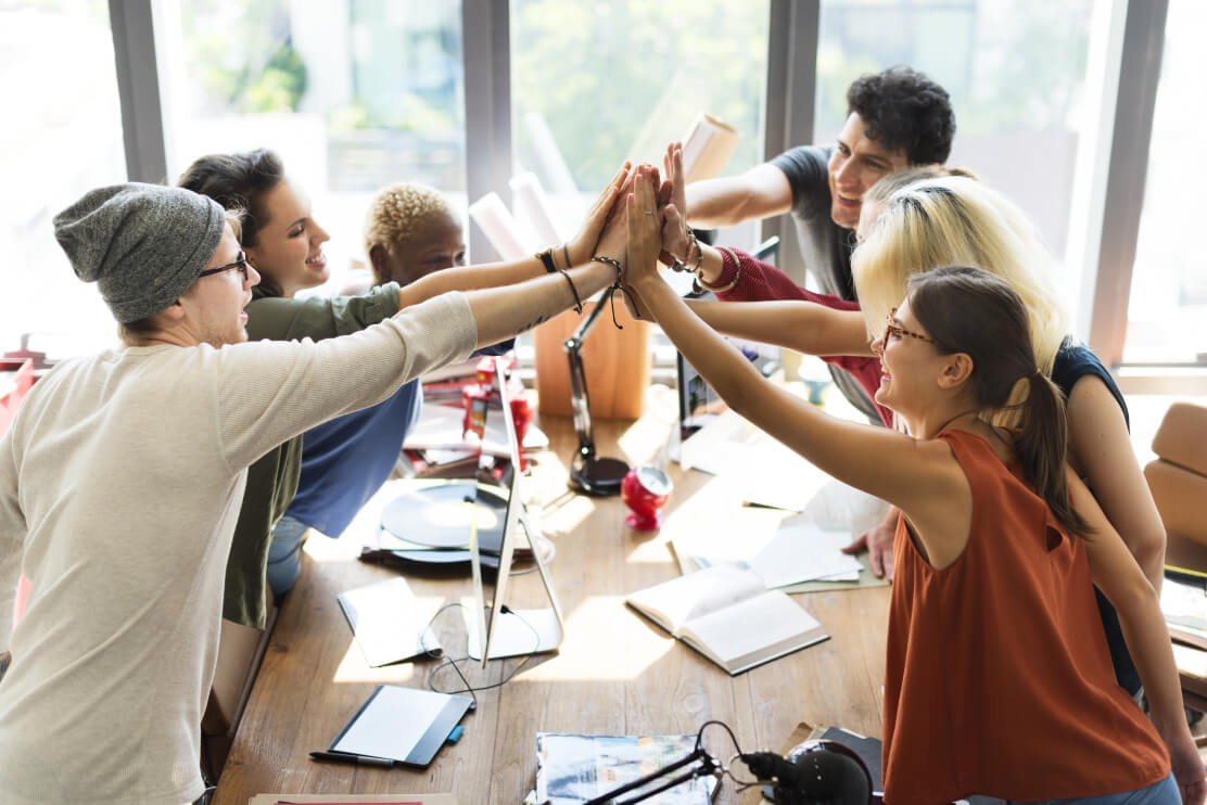 A team of colleagues in an office celebrating success by exchanging high fives.