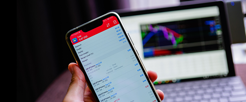 A trader, equipped with both a mobile and a laptop displaying MetaTrader 4, is prepared for trading from anywhere.