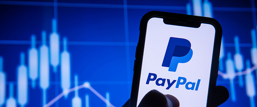 Someone holding a mobile phone with the PayPal logo, with financial charts in the background, combining payment and finance.