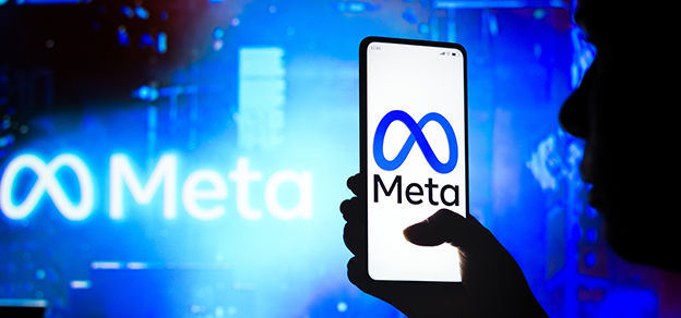 A user holding a mobile with Meta logo on the screen, and the Meta sign with a blue background behind.