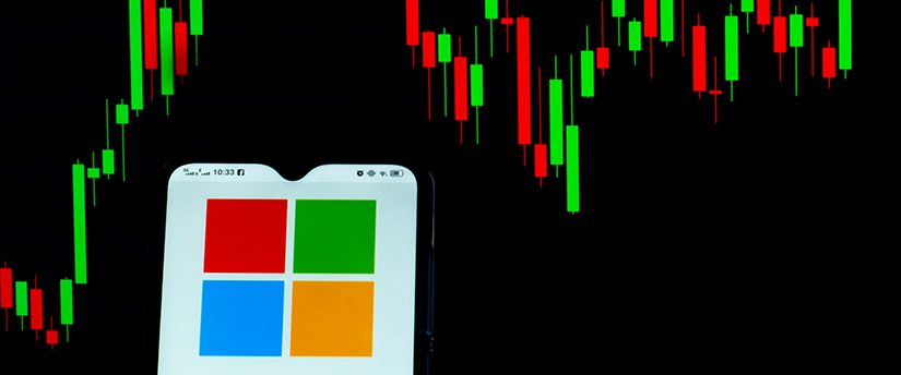 Microsoft logo on a mobile phone against candlestick charts showing Microsoft stock price movements