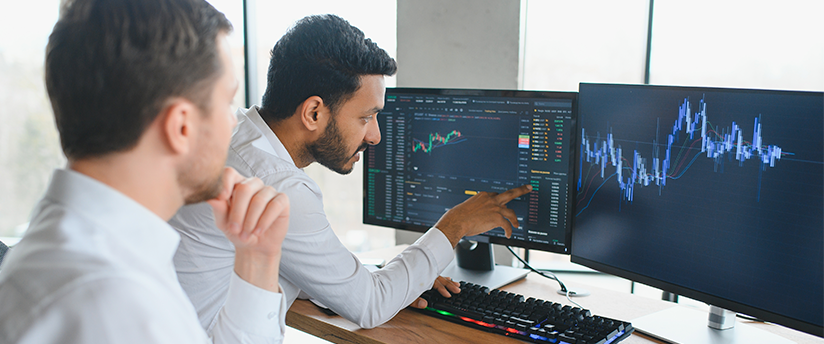 Two traders in front of screens analyzing data, exemplifying the analytical aspect of trading forex.
