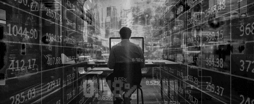 A trader seated in front of a PC with numbers surrounding him, engaged in the world of CFDs