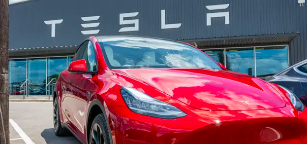 A sleek Tesla vehicle positioned beneath the distinctive Tesla sign.