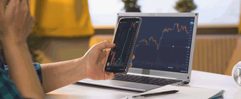 A person using a laptop and a mobile phone to trade forex, aiming to make money and achieve success in the financial market.