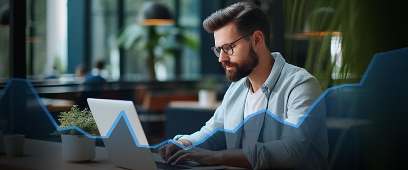 A man with a beard and glasses focused on his laptop, engaged in day trading analysis.