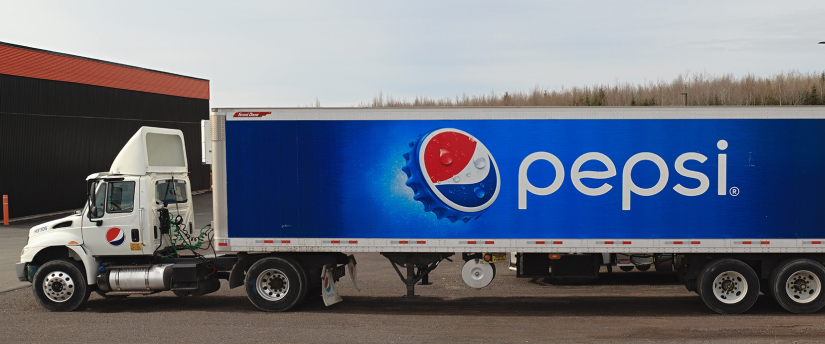 A Pepsi truck parked in front of a building. The iconic Pepsi logo is prominently displayed on the truck's exterior.