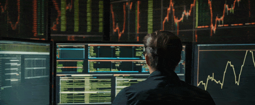 A man analyzing stock market data on multiple screens displayed on a screen.