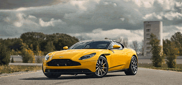 A luxurious yellow Aston Martin car gracefully drives along the road.