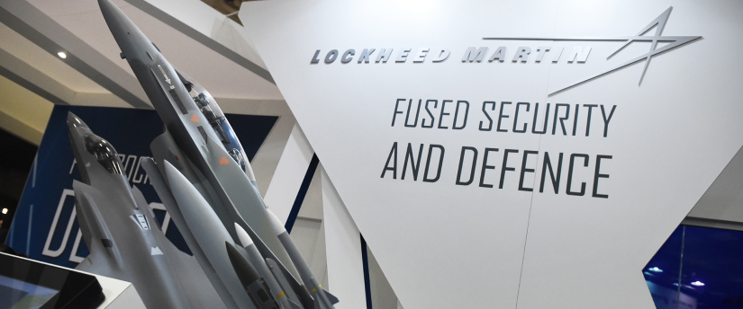 Lockheed Martin Sign: Gracefully Engraved in Glass, Backdropped by a Fleet of Sturdy Airplanes, Symbolizing Aerospace Excellence.