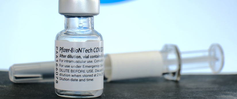 Pfizer vaccine vial with label, needle, and syringe on white background.