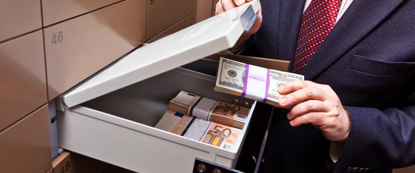 Businessman in formal attire unlocking a safe full of cash
