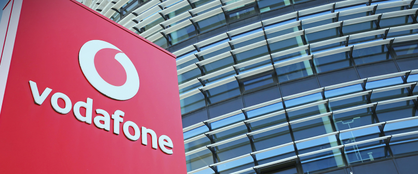 Modern Vodafone building with glass facade and logo on top, surrounded by greenery