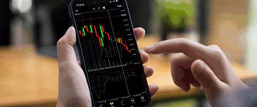 A woman trading CFD on her mobile device with multiple monitors in the background.