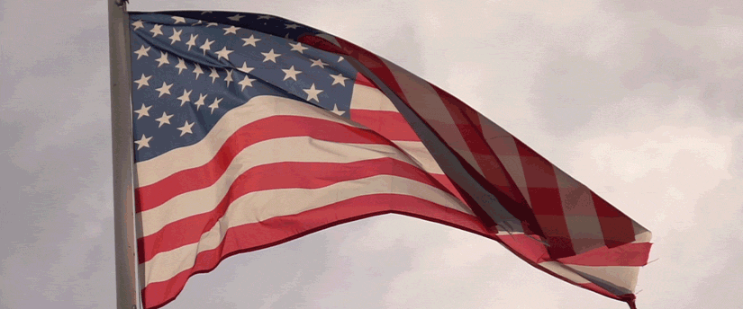 American flag waving in the wind with Donald Trump shooting in the background.