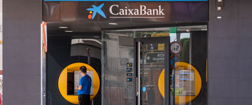 A man stands confidently in front of a modern bank building, showcasing a professional demeanor and attire.