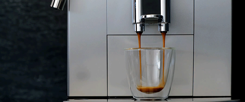 A sleek coffee machine beside a glass filled with freshly brewed coffee, showcasing a modern kitchen setting.