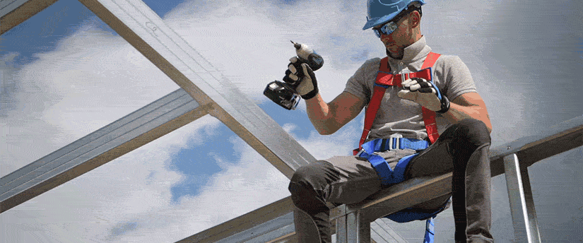 A man seated on a metal roof, holding a tool, focused on his work in a bright outdoor setting.