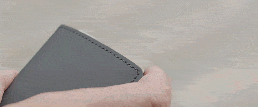 A person is holding a gray wallet that has a small hole, showcasing its worn condition.