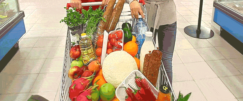A woman navigating a shopping cart brimming with food items in a grocery store.