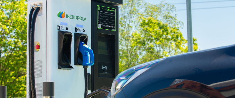 A blue car is connected to an electric vehicle charging station, indicating it is in the process of charging.