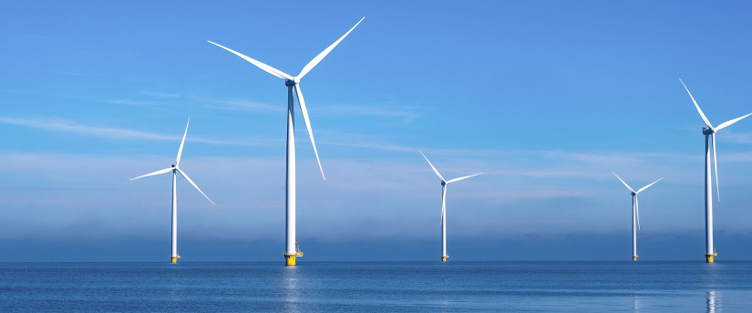A serene view of wind turbines standing tall in the ocean, harnessing renewable energy against a clear blue sky.