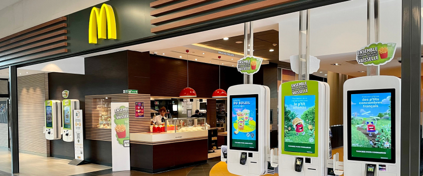 A McDonald's restaurant featuring a large screen and a self-service kiosk for ordering food.