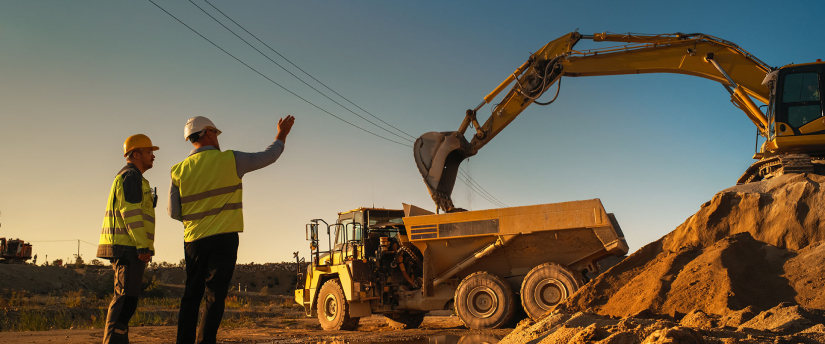 Two construction workers standing next to a large excavator, collaborating on a project at a construction site.
