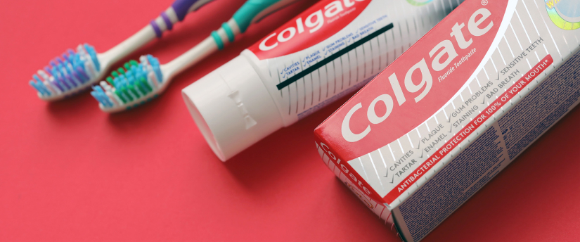 Colgate toothpaste and a toothbrush are showcased on a striking red background, representing essential oral care items.