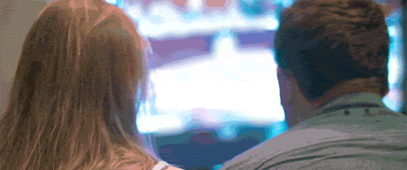 A man and a woman sitting together, engrossed in a television show, sharing a moment of entertainment and connection.
