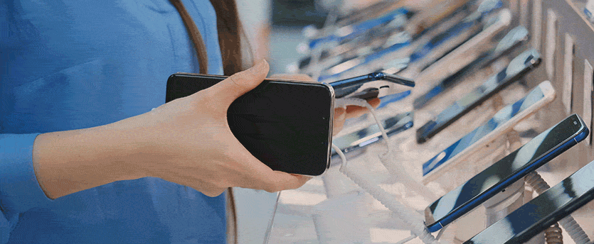 A person holds a cell phone in front of a display rack filled with various cell phones.