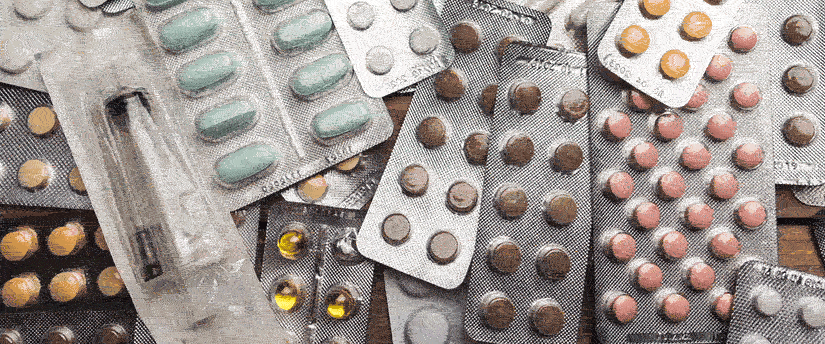 A close-up view of a disorganized pile of various pills and tablets scattered on a wooden table surface