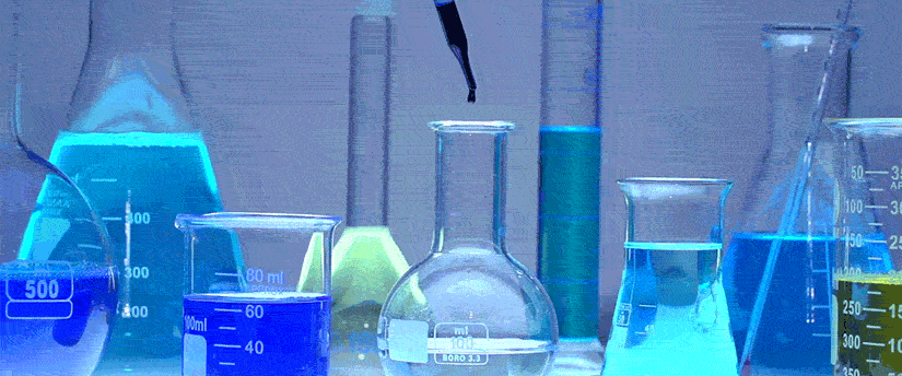 A collection of glass beakers filled with vibrant, colorful liquids arranged on a laboratory table.