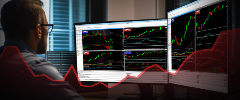 A focused man analyzing stock market graphs on a computer screen, surrounded by financial documents.