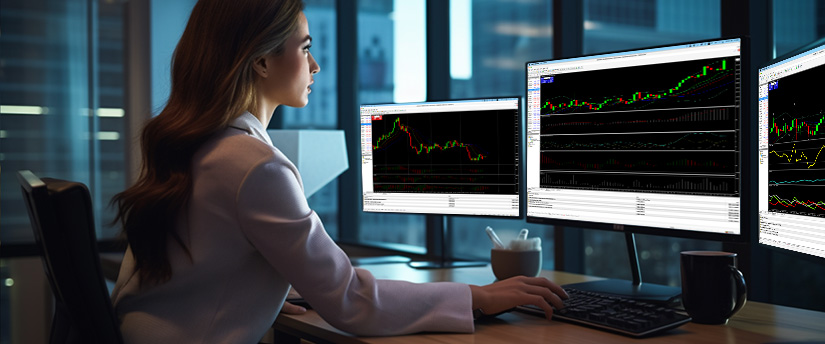 A woman at a desk with three monitors displaying various stock market graphs and data analysis