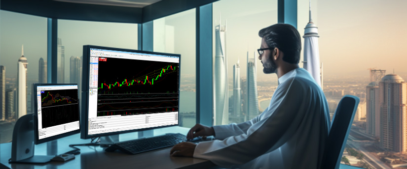 A man at a desk with two monitors displaying stock market data and charts, focused on his work.
