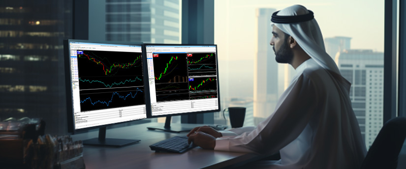 A man in traditional Arabic attire sits at a desk with two monitors showing various trading indicators and data.