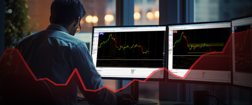 A man at a desk with two monitors displaying stock market graphs and data analysis.