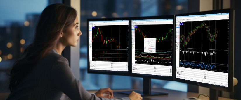 A woman focused on a computer screen displaying stock market data and graphs, analyzing financial information.