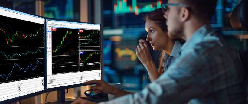 Two forex traders analyzing trading data on a computer screen, focusing on trading psychology and market trends.