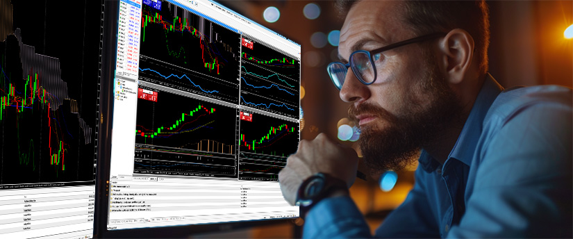 A man with glasses and a beard focused on a computer screen, reflecting on daily habits for better trading strategies.